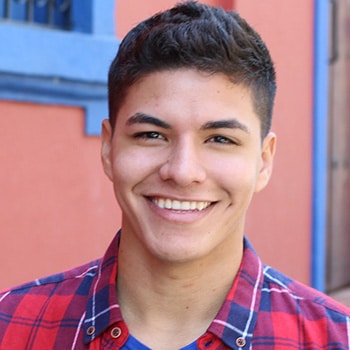 Young man smiling at camera wearing red plaid shirt against colorful blue and coral background.