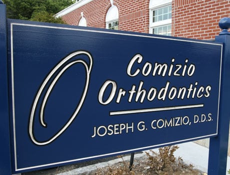 Comizio Orthodontics business sign with dentist name Joseph G. Comizio, D.D.S. displayed on brick building background.