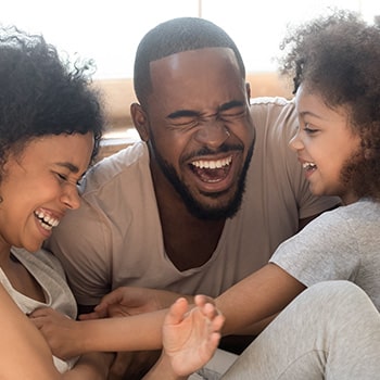 Father and two children laughing together, putting hands together in unity gesture indoors.
